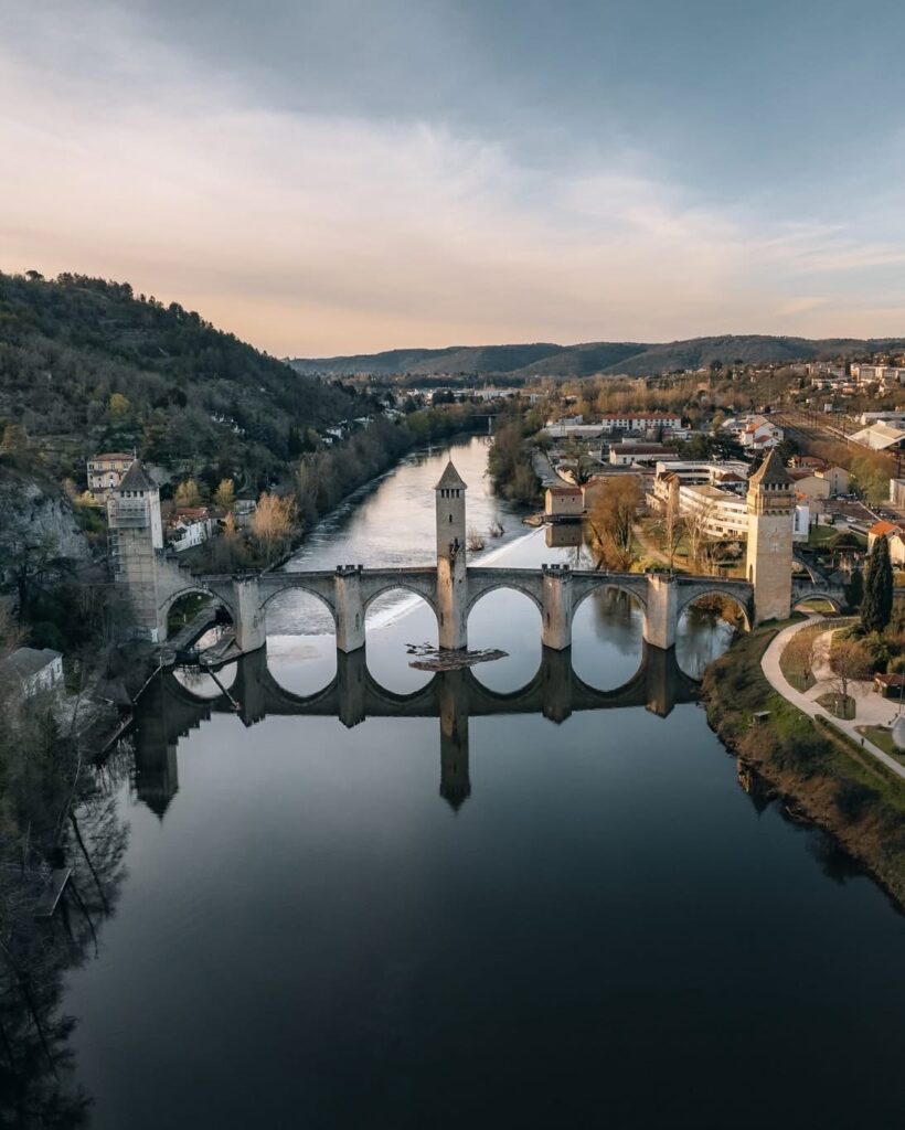 Pont Valentré viewed from a hilltop in the late afternoon, with its medieval towers reflected on the calm Lot River.