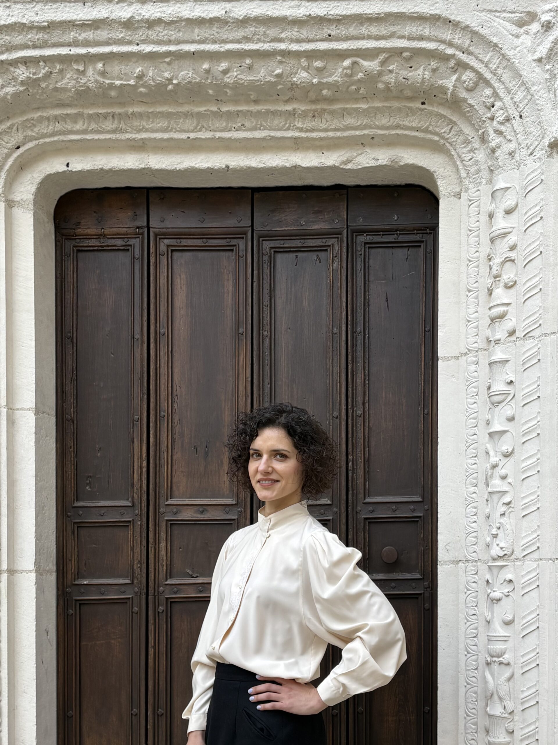 Portrait of Olga Belobrova standing on the steps beneath a medieval stone archway in Cahors, blending personal presence with historic architecture.