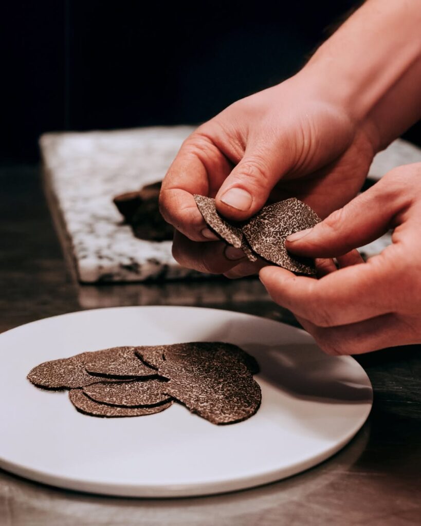 Fresh black truffle being finely sliced onto a gourmet plate during truffle season in the Lot Valley, France